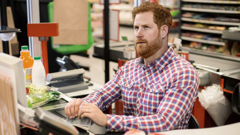 Prinz Harry sitzt an einer Supermarkt-Kassa und schaut demotiviert