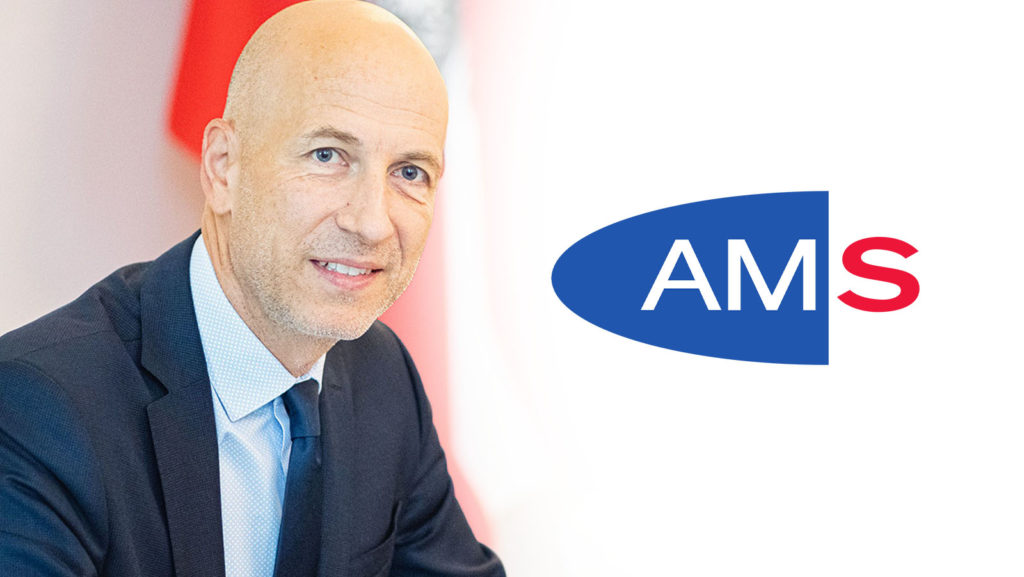 Kocher posiert vor einem Logo des Arbeitsmarktservice