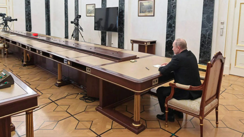Putin sitzt an langem Tisch mit rotem Knopf an anderem Ende