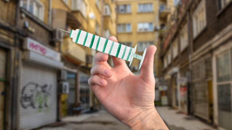 Eine Hand hält eine Gmundner Heroinspritze in einer dunklen Gasse
