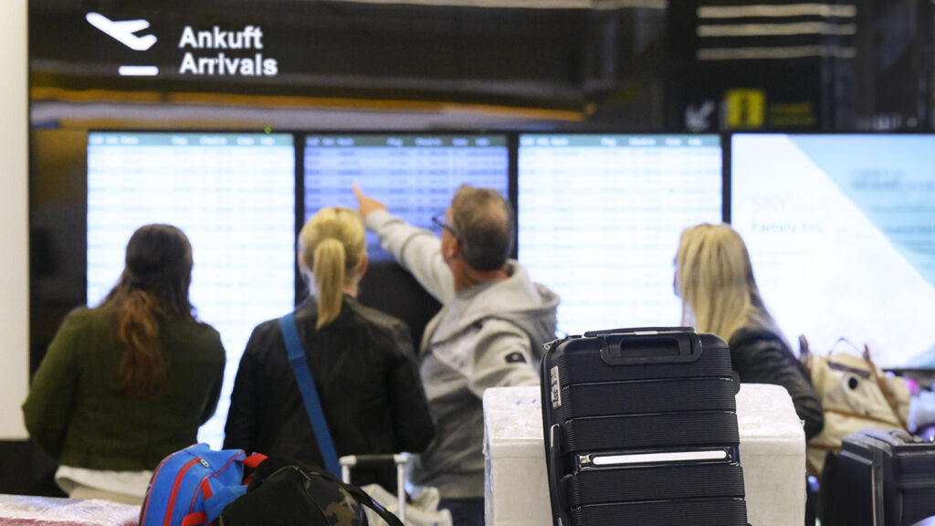 Menschen stehen vor Ankunft-Bildschirm am Flughafen