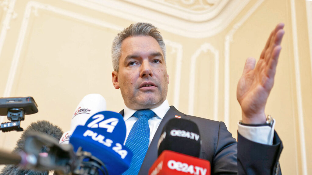 Karl Nehammer gestikuliert eine Watsche vor Mikrofonen