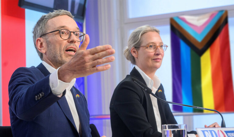 Herbert Kickl und Alice Weidel bei einer Pressekonferenz, im Hintergrund hängt eine Pride-Flagge