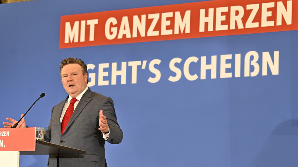 Michael Ludwig vor einem Banner mit der Aufschrift „Mit ganzem Herzen, geht's scheißn"