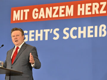 Michael Ludwig vor einem Banner mit der Aufschrift „Mit ganzem Herzen, geht's scheißn"