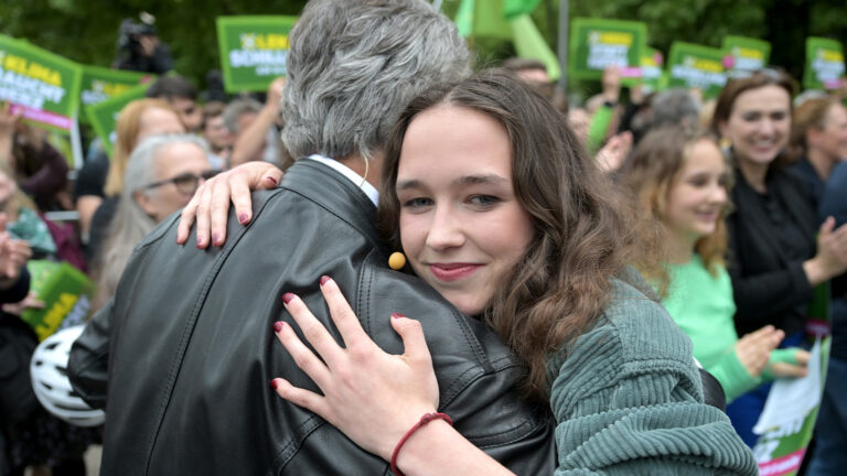 Lena Schilling umarmt Werner Kogler und lächelt dabei verschmitzt.