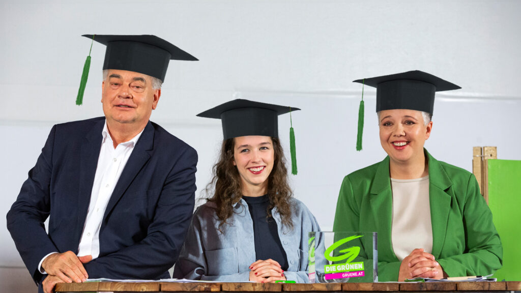 Kogler, Schilling und Voglauer mit Abschlusshüten bei einer Pressekonferenz