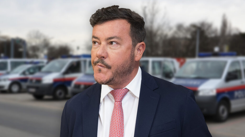 Benko blickt apathisch an der Kamera vorbei, hinter ihm Polizeiautos.