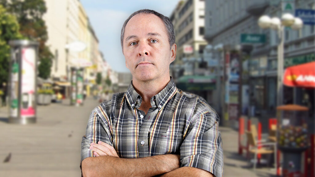 Ein älterer Herr mit finsterer Miene und verschränkten Armen posiert auf der Favoritenstraße in Wien.