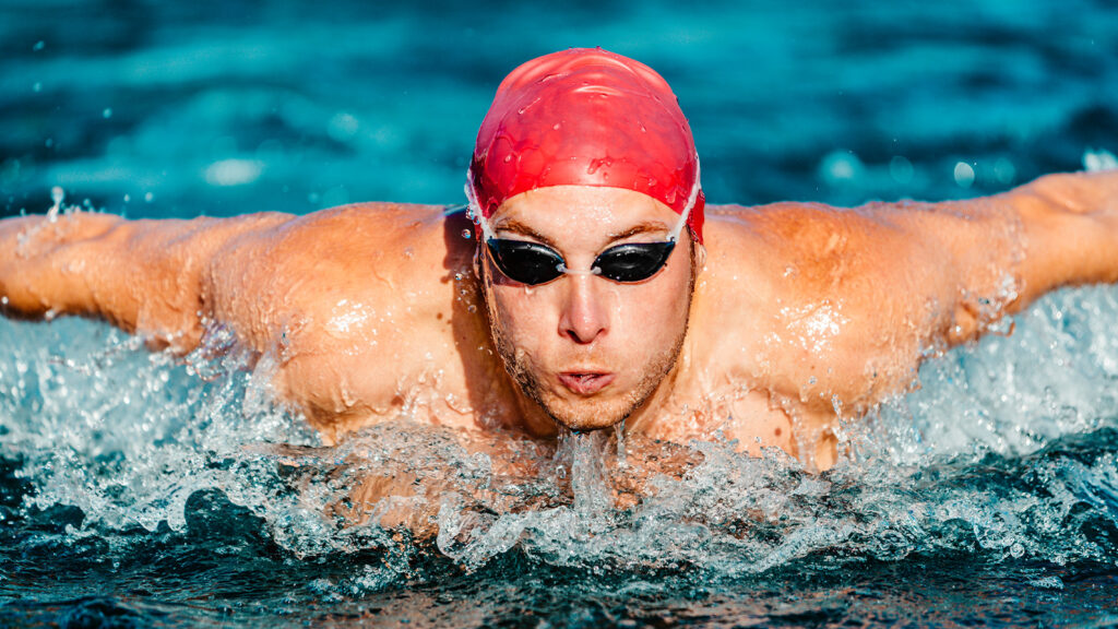 Ein Schwimmer mit verkrampften Gesicht krault sich durch ein Schwimmbecken.