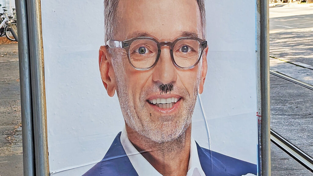 Das Bild zeigt ein Plakat mit Herbert Kickl und einem aufgemalten Hitlerbärtchen.
