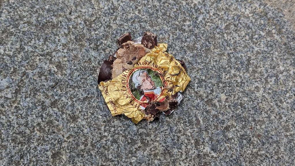 Das Bild zeigt eine flach gedrückte Mozartkugel auf einem Gehsteig.