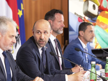 Das Bild zeigt eine Pressekonferenz, im Hintergrund läuft Tom Turbo.