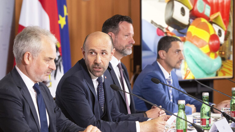 Das Bild zeigt eine Pressekonferenz, im Hintergrund läuft Tom Turbo.