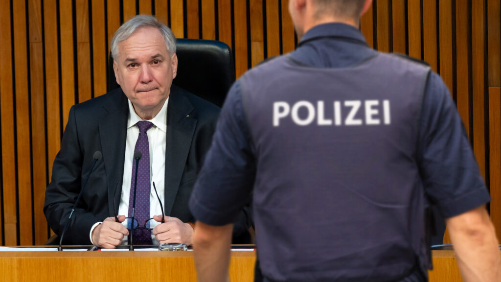 Das Bild zeigt einen Polizisten im Hintergrund sitzt Rosenkranz