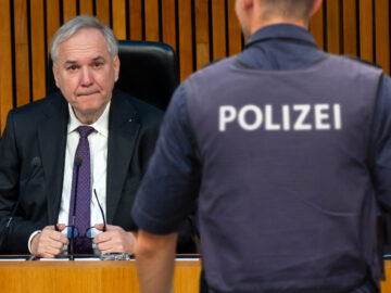 Das Bild zeigt einen Polizisten im Hintergrund sitzt Rosenkranz