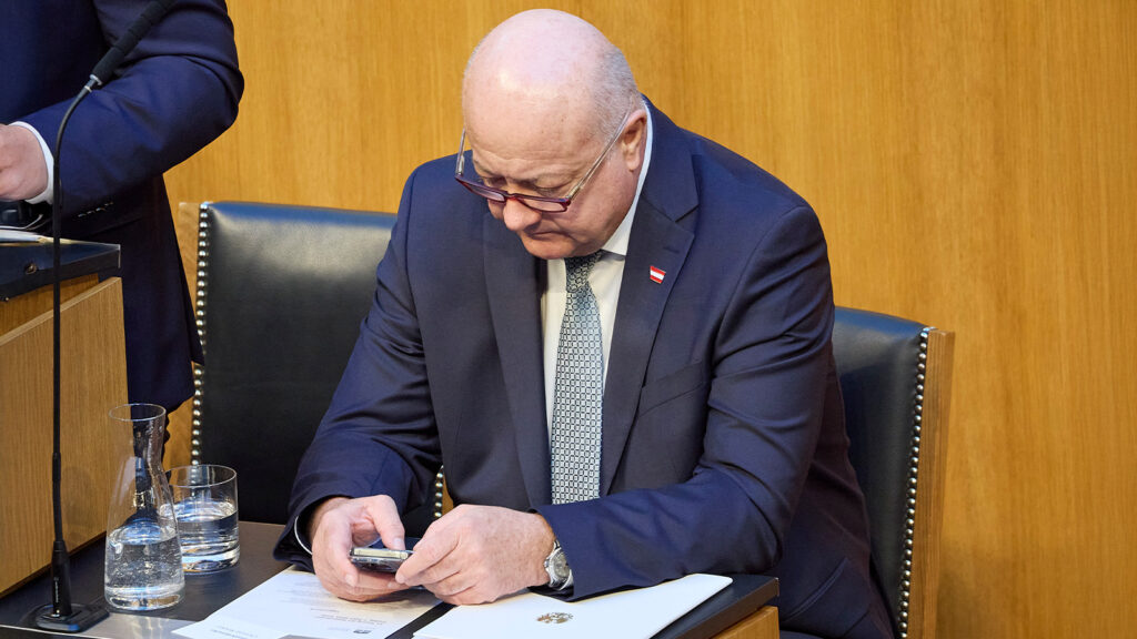 Das Bild zeigt Christian Stocker wie er verwundert auf sein Handy blickt.