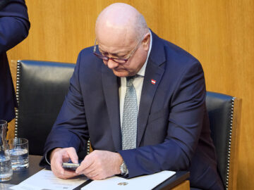 Das Bild zeigt Christian Stocker wie er verwundert auf sein Handy blickt.