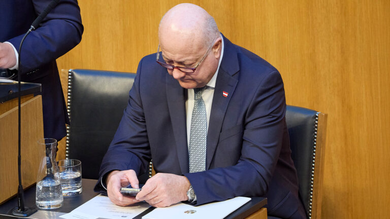 Das Bild zeigt Christian Stocker wie er verwundert auf sein Handy blickt.