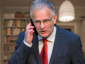 Das Bild zeigt Marterbauer am Telefon in seinem dunklen Wohnzimmer.