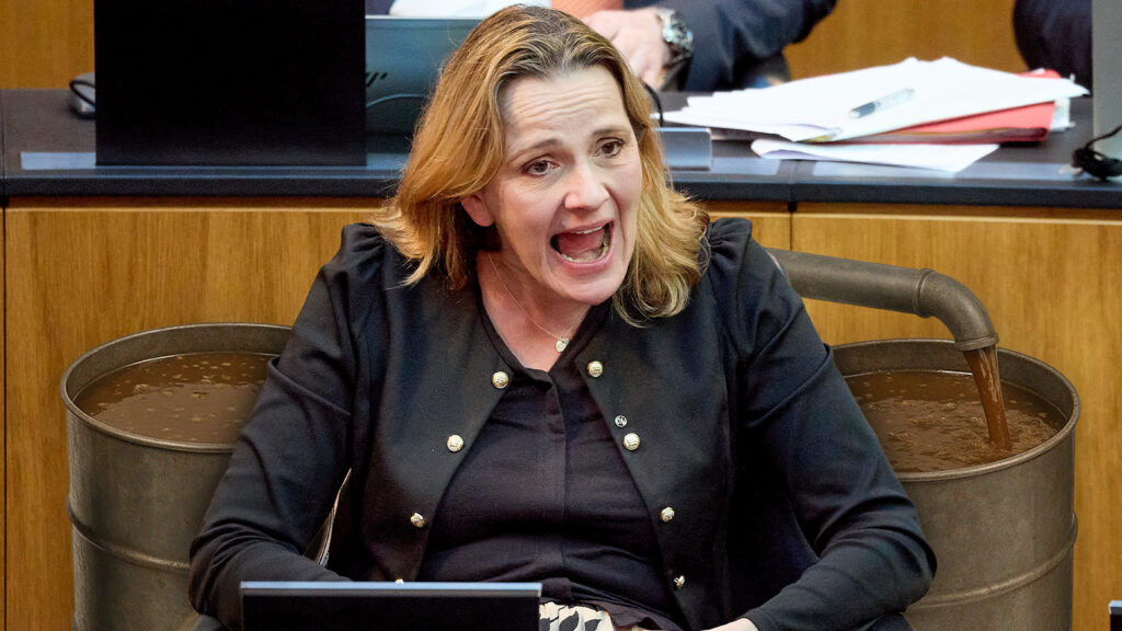 Das Bild zeigt Belakowitsch mit zwei Fässern mit brauner Flüssigkeit im Parlament.