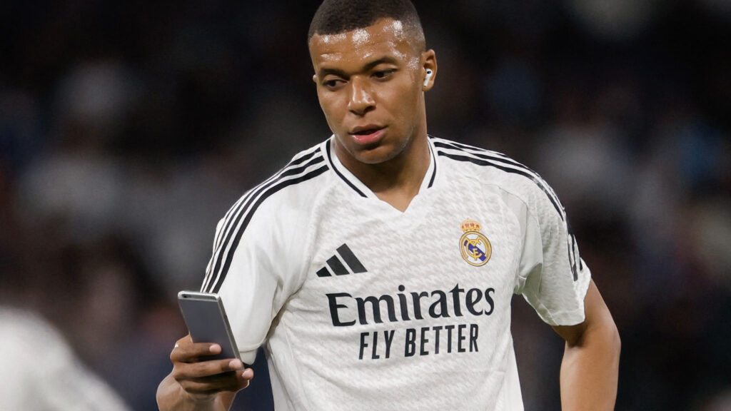 Mbappé steht am Spielfeld und schaut auf sein Handy