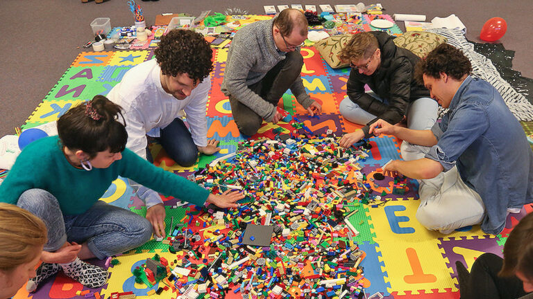 Das Bild zeigt eine Gruppe Erwachsener, die am Boden mit Lego spielt.