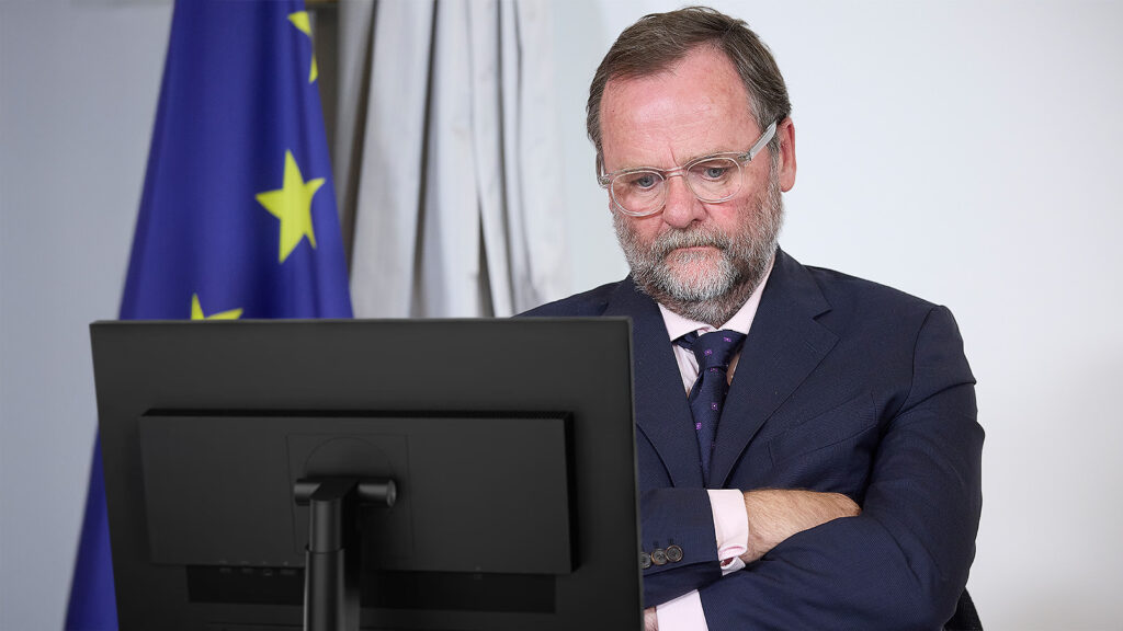 Das Bild zeigt Sepp Schellhorn mit demprimierten Blick und verschränkten Armen vor einem PC Bildschirm.