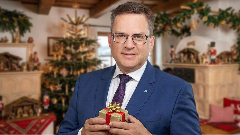 Das Bild zeigt Wöginger in einem weihnachtlich dekorierten Wohnzimmer mit einem kleinen Geschenk in der Hand.