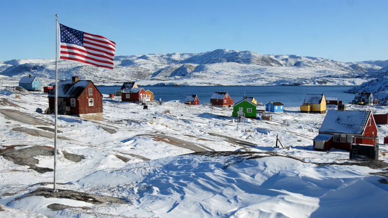 Das Bild zeigt ein Dorf in Grönland. Am linken Bildrand prangt eine US-Flagge.