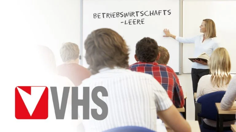 Das Bild zeigt das VHS Logo und eine Klasse voller Menschen.