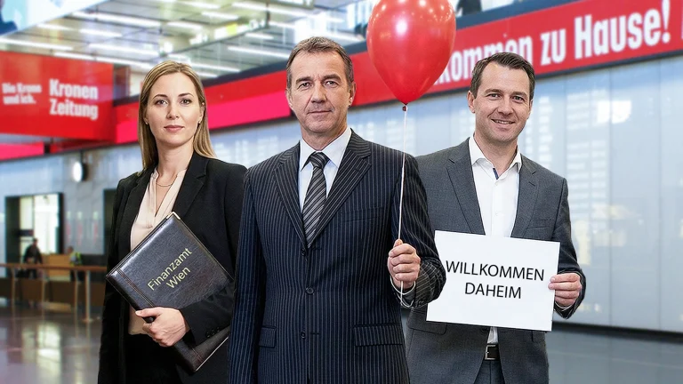 Das Bild zeigt drei Personen im Anzug in der Ankunfthalle am Flughafen Wien Schwechat. Sie halten eine Mappe, einen Ballon und ein Schild mit der Aufschricht "Willkommen Daheim".
