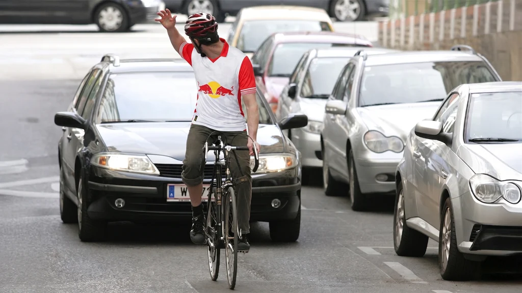 Das Bild zeigt einen Radfahrer im Red Bull Trikot vor einem Auto auf einer Wiener Straße.