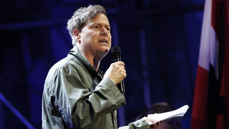 Das Bild zeigt den Intendant der Wiener Festwochen Milo Rau mit einer Liste in der Hand auf einer Bühne.