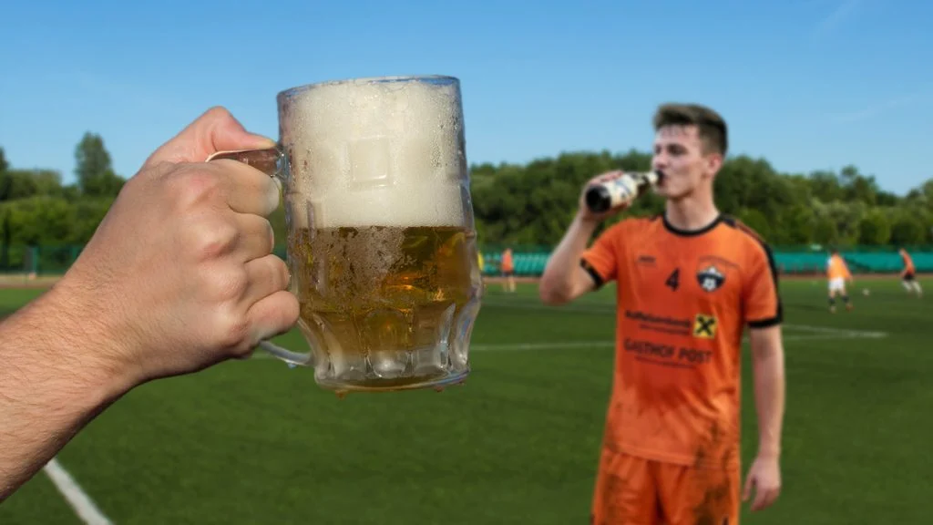 Das Bild zeigt eine Hand mit Bierkrug, im Hintergrund sieht man verschwommen einen dorfsportplatz und einen Spieler mit einem Bier in der Hand.