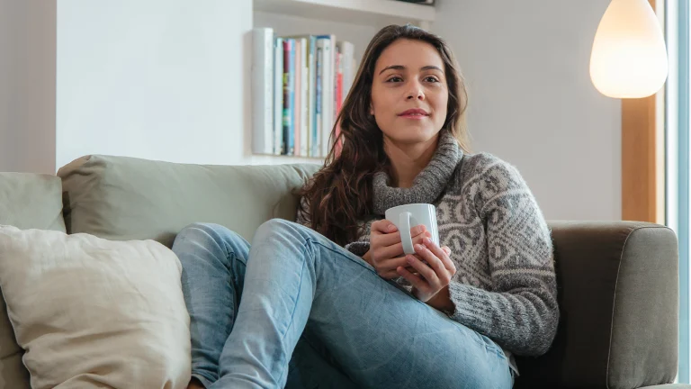 Das Bild zeigt eine Frau, die auf der Couch sitzt und fernschaut.