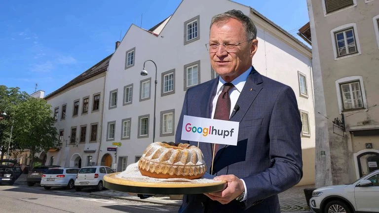 Das Bild zeigt Landeshauptmann Stelzer mit einem Guglhupf vor Hitlers Geburtshaus. Aus dem Guglhupf ragt eine Fahne mit der Aufschrift "Googlehupf".
