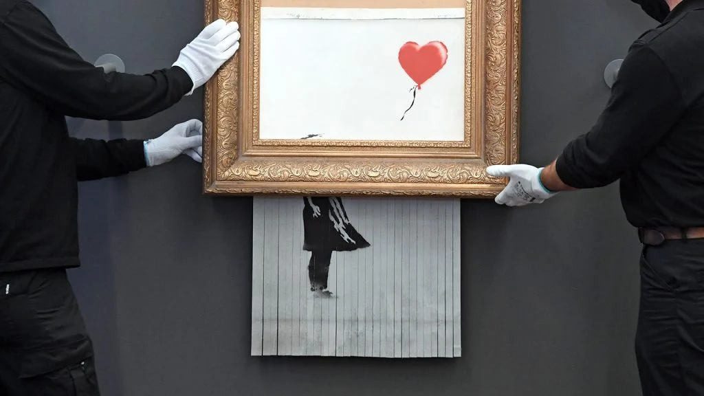 Das Bild zeigt das Banksy Kunstwerk "Mädchen mit rotem Ballon", wie es gerade geschreddert wird.