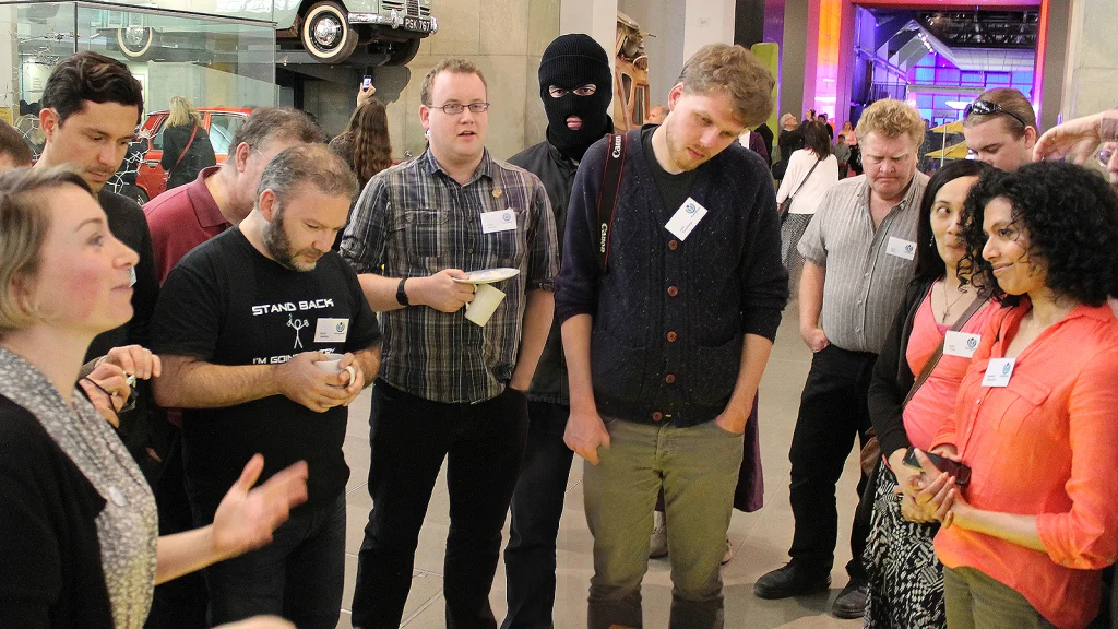 Das Bild zeigt eine Gruppe im Museum. Hinter der Gruppe steht ein Mann mit Sturmhaube.