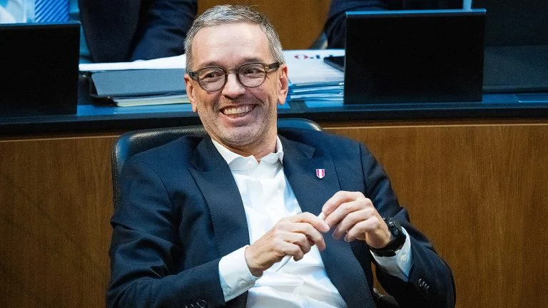 Das Bild zeigt einen lachenden Herbert Kickl, der zurückgelehnt im Parlament sitzt.